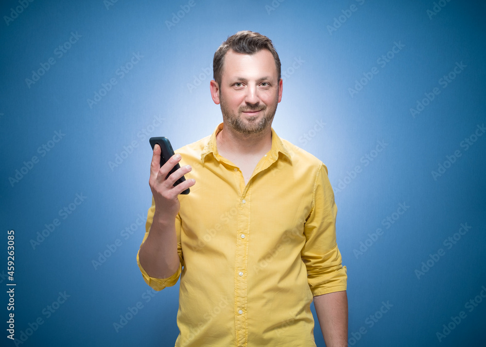 Happy man with phone over blue background, dresses in yellow shirt. Copy space for text. Trendy happy guy using mobile phone Happy man with phone over blue background, dresses in yellow shirt. Copy space for text. Trendy happy guy using mobile phone