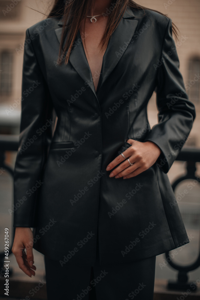 Female hands with silver rings in the pockets of a black long leather jacket. Style, design of women's clothing. Vertical