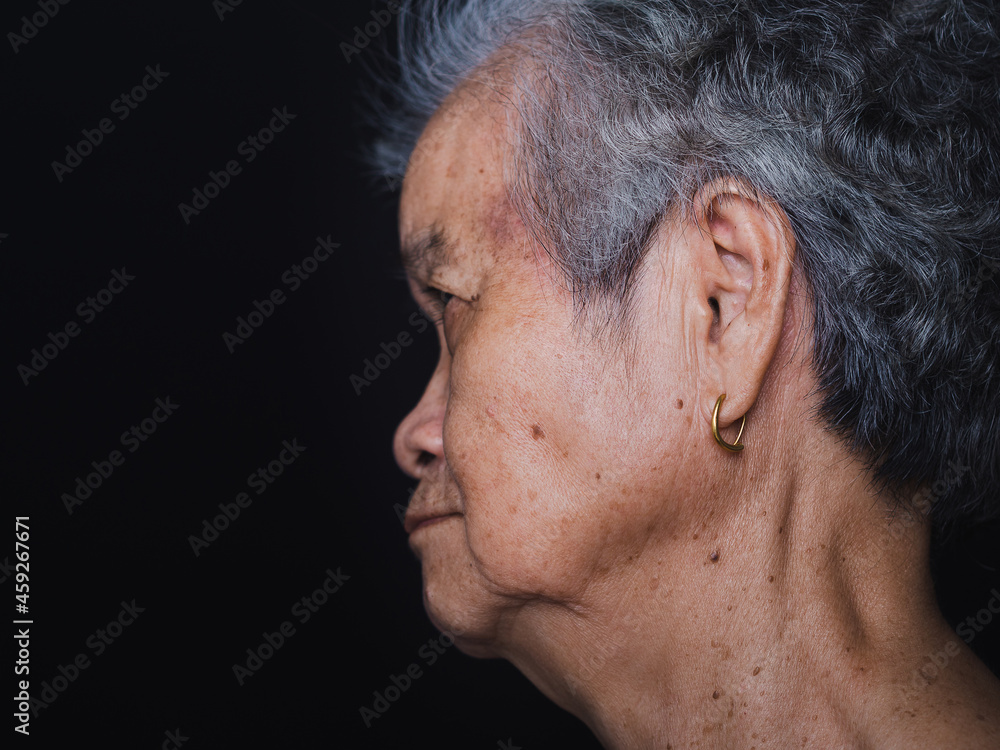 Obraz premium Side view of an elderly Asian woman with short gray hair and looking away while standing with a black background in the studio. Close-up photo. Aged people and health care concept