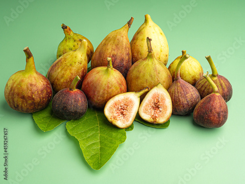 A pile of ripe figs fruit is on green leaves isolated on a green background. High Vitamins fruit. Close-up photo. Space for text. Healthy fruits and healthcare concept photo