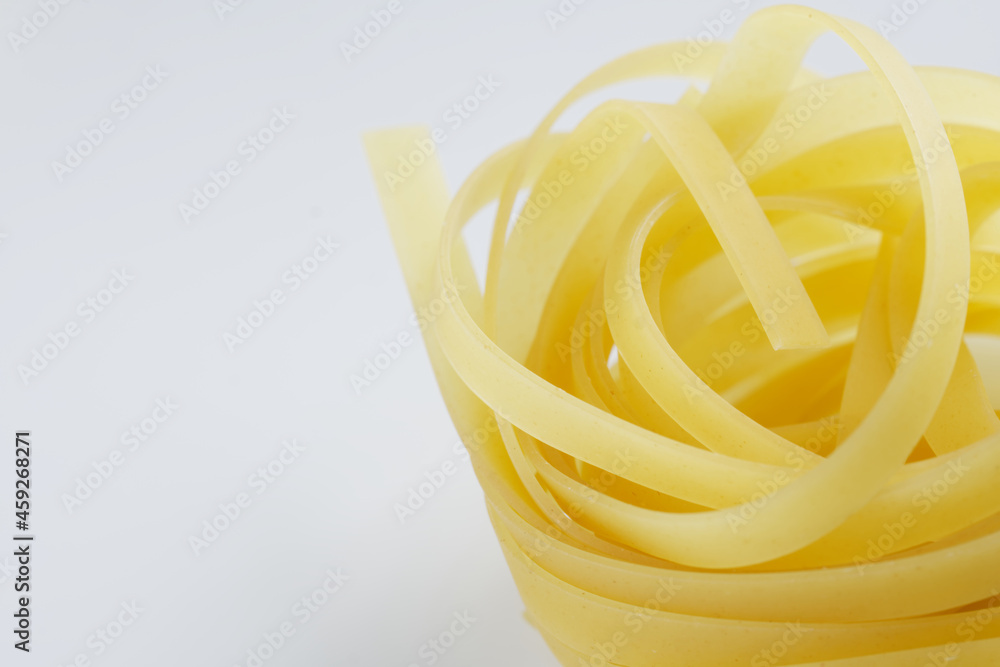 A nest of fettuccine pasta made from durum wheat lies on a white surface. Cooking food. Macro. Selective focusing. Daylight A nest of fettuccine pasta made from durum wheat lies on a white surface. Cooking food. Macro. Selective focusing. Daylight