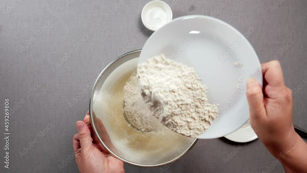 woman pours flour into a sieve and sifts it into the dough top view close-up woman pours flour into a sieve and sifts it into the dough top view close-up