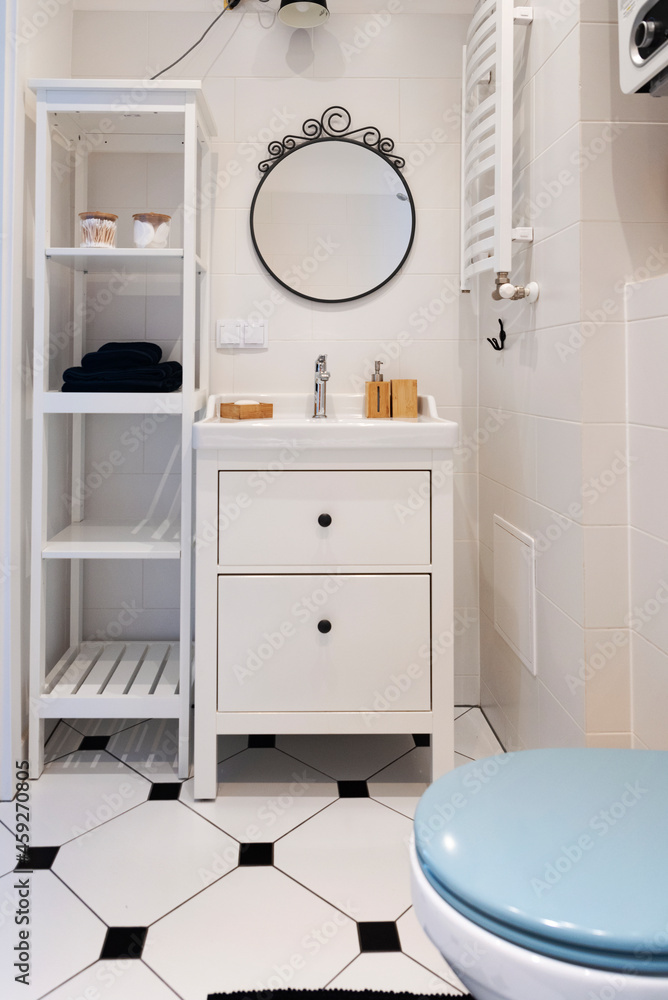 Small bathroom with stylish tiles on the floor, white cabinet, toilet and round mirror on the wall. Interior of bathroom in scandinavian design. Vertical Small bathroom with stylish tiles on the floor, white cabinet, toilet and round mirror on the wall. Interior of bathroom in scandinavian design. Vertical