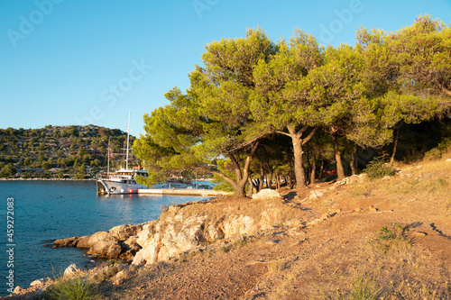 Rocky beach, pine trees and boat moored by the pier in summer sunset on Murter island, Croatia photo
