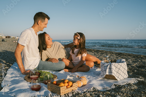 Family spending time together outdoor. Picnic lunch with fruits by the seaside. Happy people eating healthy food and sitting on blanket on the beach. Summer leisure concept.