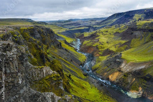 Woman hiker enjoying Highlands of Iceland. River Fossa stream in the Landmannalaugar canyon valley. Hills and cliffs are coverd by green moss