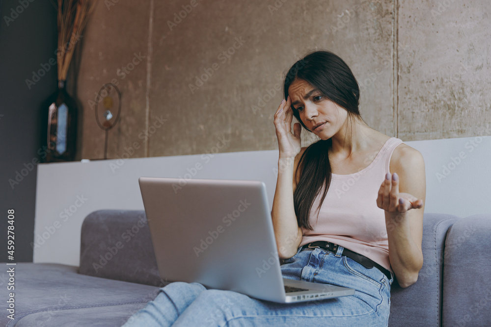 Upset frowning distempered young latin woman 20s in casual clothes sit on sofa hold use talk work on laptop pc computer get video call hold head with hand spend time in living room home in own house. Upset frowning distempered young latin woman 20s in casual clothes sit on sofa hold use talk work on laptop pc computer get video call hold head with hand spend time in living room home in own house.