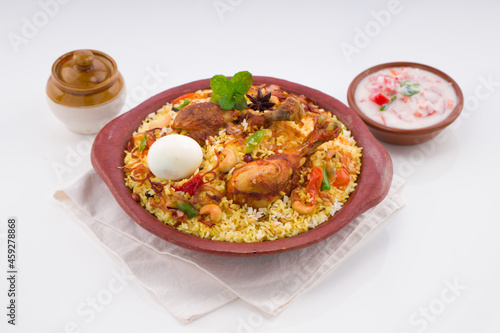 Chicken biryani , kerala style chicken dhum biriyani made using jeera rice and spices arranged in earthen ware with raitha and lemon pickle as side dish on white background, isolated