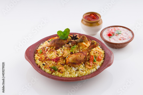 Chicken biriyani , kerala style chicken dhum biriyani made using jeera rice and spices arranged in earthen ware with raitha and lemon pickle as side dish on white background, isolated