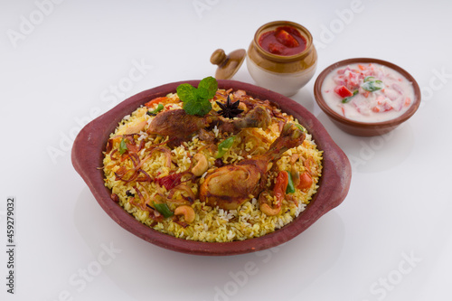 Chicken biriyani , kerala style chicken dhum biriyani made using jeera rice and spices arranged in earthen ware with raitha and lemon pickle as side dish on white background, isolated
