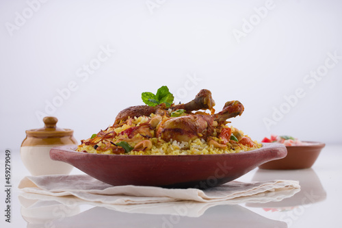 Chicken biriyani , kerala style chicken dhum biriyani made using jeera rice and spices arranged in  earthen ware with raitha and lemon pickle as side dish on white background, isolated