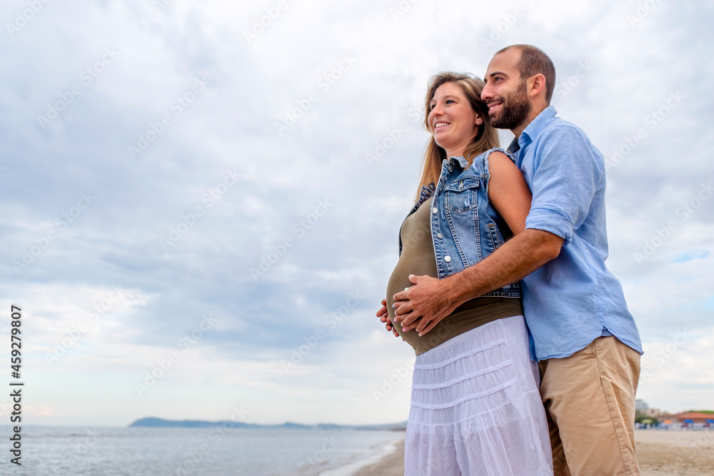 young happy couple in love of a pregnant woman and her boyfriend hugging on the beach having fun on holidays. quality family time holding hands on big belly on vacation days. joy and lifestyle concept young happy couple in love of a pregnant woman and her boyfriend hugging on the beach having fun on holidays. quality family time holding hands on big belly on vacation days. joy and lifestyle concept