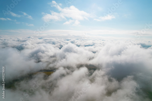 Cumulus clouds, aerial background. Aerial shot with top view of white fluffy clouds gathering. In between the clouds the ground is visible here and there.