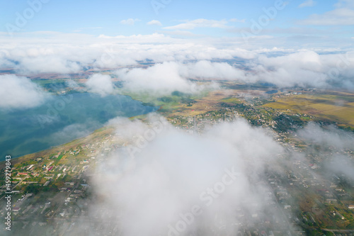 Cumulus clouds, aerial background. Aerial shot with top view of white fluffy clouds gathering. In between the clouds the ground is visible here and there. © Elena
