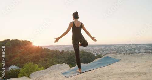 Back view of the mindful peaceful caucasian woman with a calm look meditates outdoor  while keeping hands in namaste gesture. Female trying to relax at the nature