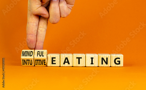 Mindful or intuitive eating symbol. Doctor turns cubes and changes words intuitive eating to mindful eating. Beautiful orange background, copy space. Medical and mindful or intuitive eating concept. photo