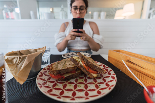 Sandwich en primer plano enfocado con chica de fondo tomando foto con smartphone photo