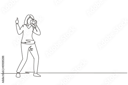 Single continuous line drawing cute woman photographer standing, thumbs up gesture, holding photo camera and photographing. Creative profession or occupation. One line draw design vector illustration