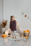 Little cute girl playing in a wigwam in her room with autumn decor and pumpkins. Happy childhood concept