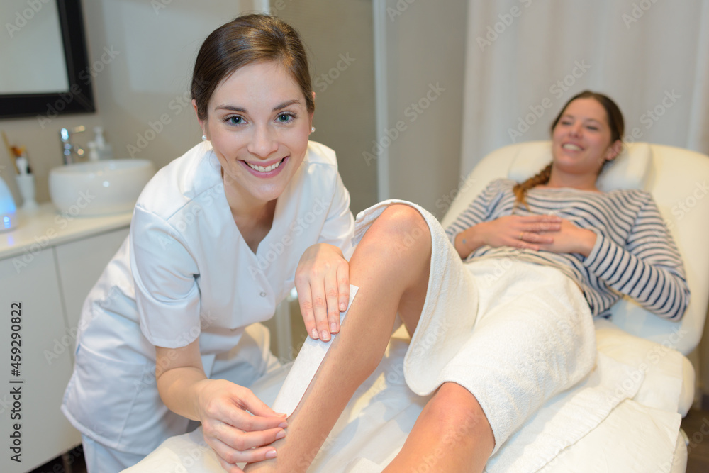 beautician poised to remove wax strip from clients leg beautician poised to remove wax strip from clients leg