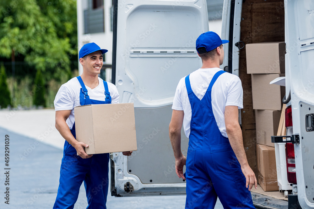 Two removal company workers unloading boxes from minibus into new home