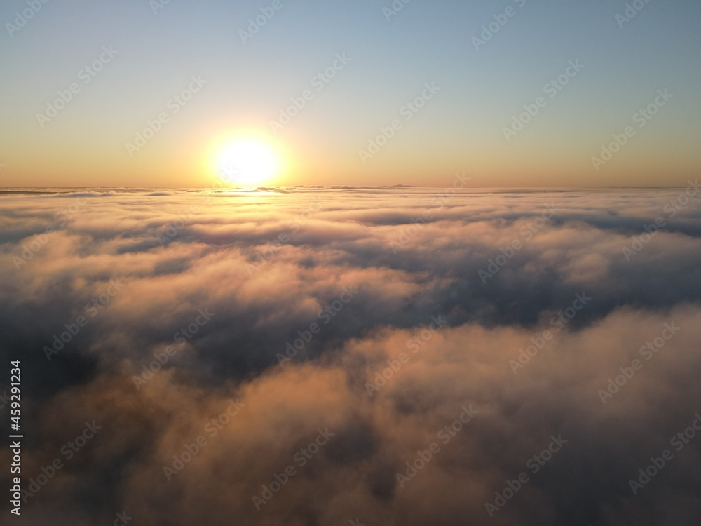 Dense fog clouds with the morning sunrise. Clouds formed over a lake approximately 100 feet below the clouds. Image could be drone an airplane window or drone.