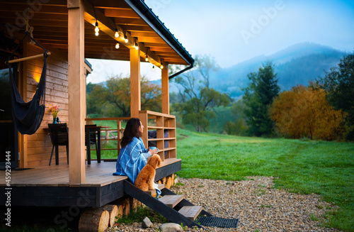  Woman with dog resting on the terrace mountain chalet at sunset.