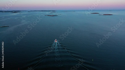 Aerial view of a sunlit boat driving away on tranquil sea water, dusk in Scandinavia - rising, drone shot photo