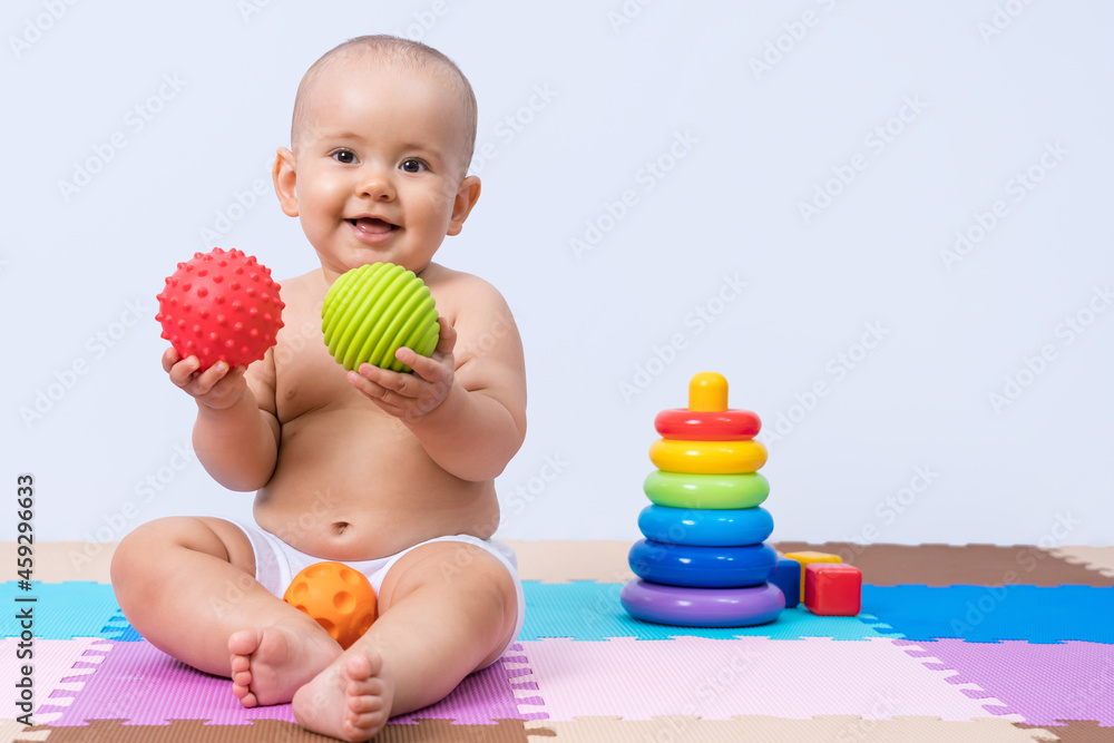 Newborn sits on the floor and plays with a green and red rubber ball Newborn sits on the floor and plays with a green and red rubber ball