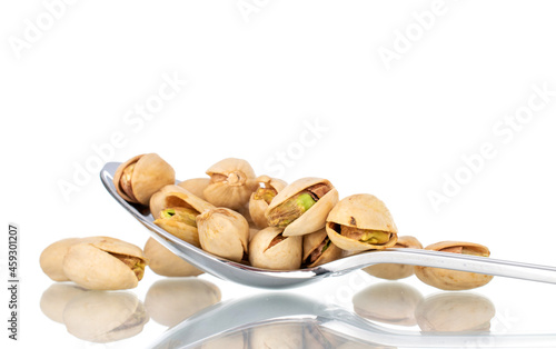 Several unpeeled pistachios with a metal spoon, close-up, isolated on white.