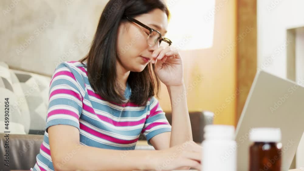 Asian woman who works at home is tired, stressed, exhausted and has a headache, cold and flu, taking capsule medicine, overworked by using laptop computers to do online business. Asian woman who works at home is tired, stressed, exhausted and has a headache, cold and flu, taking capsule medicine, overworked by using laptop computers to do online business.