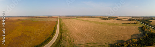 Aerial panorama of a flat prairie in autumn with harvested and unharvested fields and a road disappearing into the distance. 