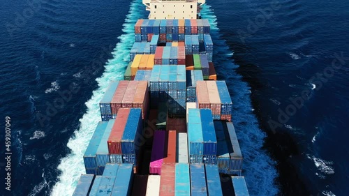 Aerial drone video above huge colourful container carrier vessel cruising deep blue open ocean sea