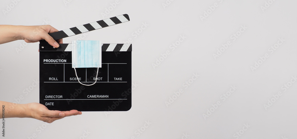 Hand is holding Clapperboard or movie slate and face mask on white background.