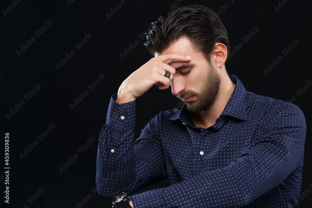 Handsome young man holds his head with his hand isolated on black background.
