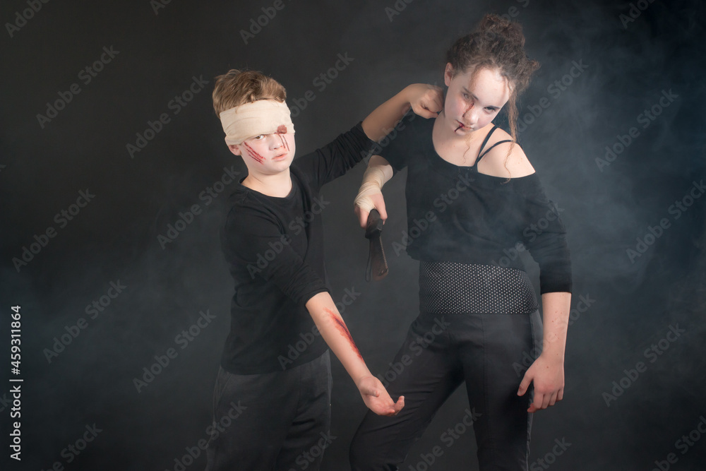 Couple of dressed up teenage kids during a machete mock fight in Halloween zombie costumes displaying a fist defence Couple of dressed up teenage kids during a machete mock fight in Halloween zombie costumes displaying a fist defence