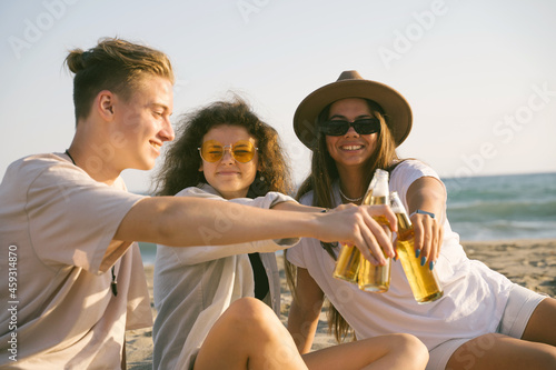 Young happy friends doing picnic seaside. Group of people sitting on the beach, eating pizza and drinking beer together. Summer spending time outdoor concept. © valeriyakozoriz