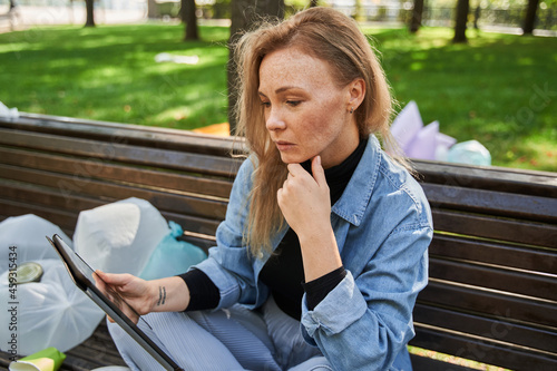 Woman being deep at her device while sitting at the bench around the rubbish photo