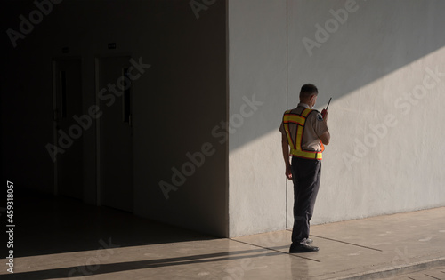 Photo Asian security guard in safety vest using walkie-talkie while working on sidewal