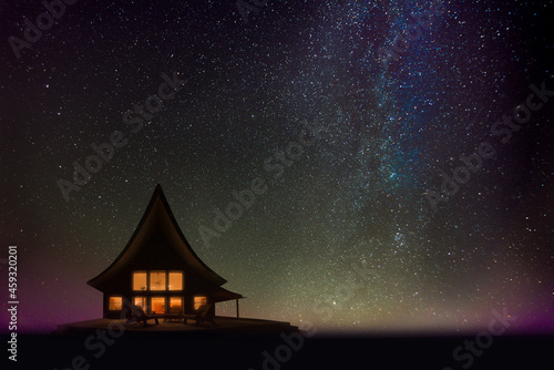 Silhouette of a cozy cabin at night overseeing Lake Superior, Upper Peninsula, Michigan, pictured against the stars of our galaxy and the earliest rays of sunrise