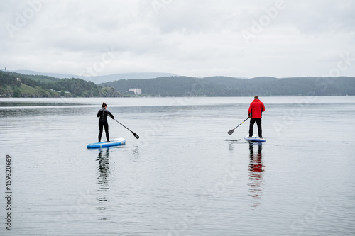 Two men stand and swim on sup boards on the lake on a cloudy day. Active rest on the lake with friends.