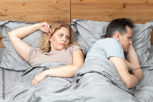 Two in bed, a woman looks with suspicion at a man who has turned away in the other direction. Relationship concept photo