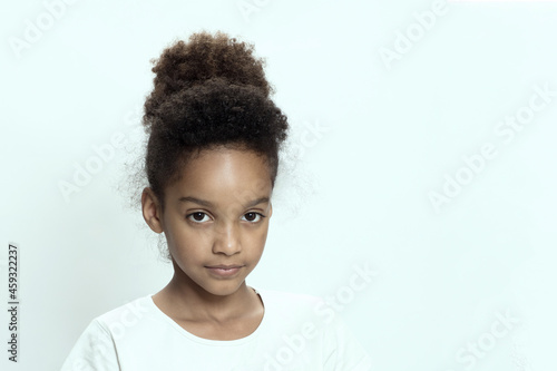 Portrait of a beautiful mixed race kid on white studio background. Beautiful young girl with afro hair. Child looks to the camera. Concept of childhood, cute schoolgirl 9-10 years old. Copy space. 