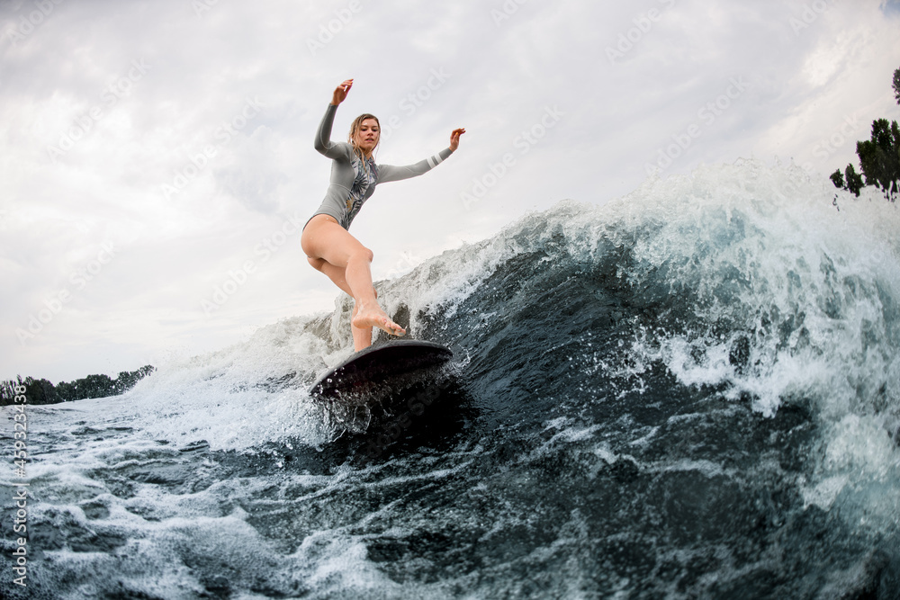 attractive woman on wakeboard rides down on wave against a cloudy sky