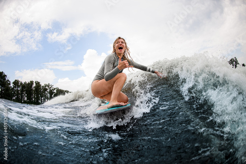 happy woman rides down the wave sitting on a wakeboard. Wakesurfing on the river. Summertime leisure