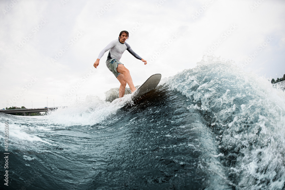 Active sportsman skilfully balancing on wave on wakesurf board.