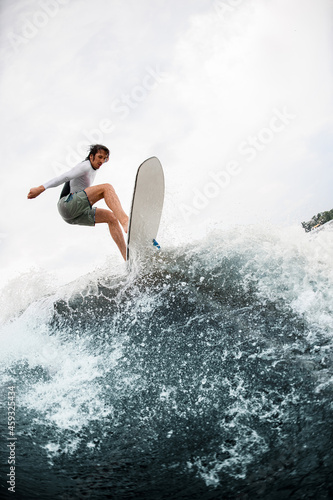 Athletic guy having fun and jumps at wave on wakesurf board in the summer day.