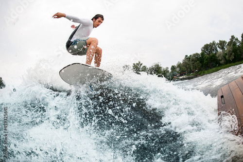 young sportsman skilfully jumps on wakeboard over splashing wave.