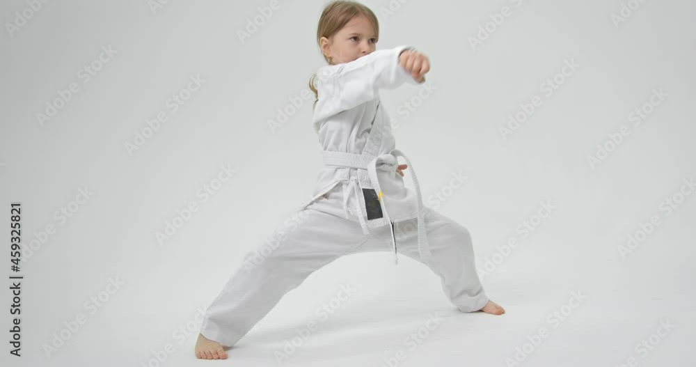 The child spreads his legs wide and strikes with straight hands in front of her. Karate exercises. The child spreads his legs wide and strikes with straight hands in front of her. Karate exercises.