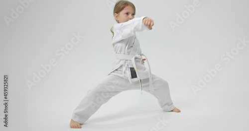 The child spreads his legs wide and strikes with straight hands in front of her. Karate exercises.